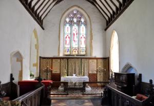 An interior picture of St Peter's Carlton showing the aisle, altar and stsained glass main window